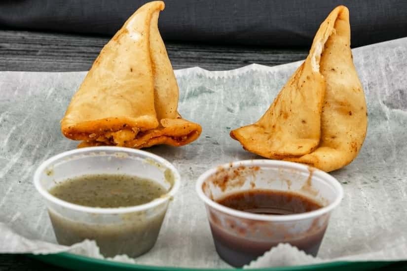Two samosas with green and tamarind chutneys